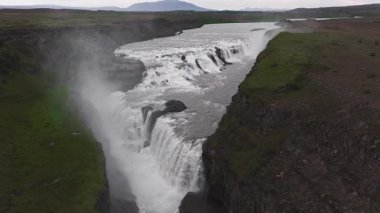 İzlanda 'daki Gullfoss şelalesi güçlü bir şekilde bir kanyona akar. Sisler yükselir ve uzak dağlar dramatik manzarayı güçlendirir..