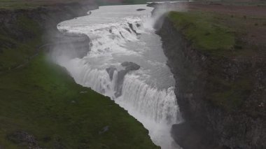 İzlanda 'daki Gullfoss şelalesinin havadan görünüşü, dinamik su akışı, sislerin yükselmesi, yeşil düzlükler, uzak dağlar ve bir izleme platformu..