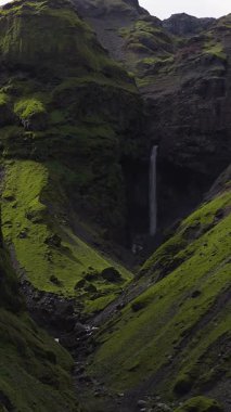 İzlanda 'daki yemyeşil bir kanyonun havadan görünüşü yosun kaplı uçurumlar, kayalık bir havzaya dökülen uzun bir şelale ve pürüzsüz kamera..