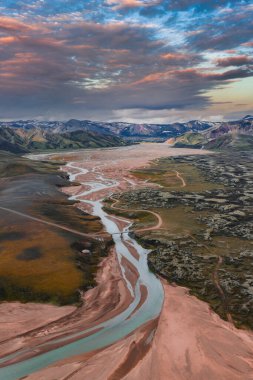 Tepeler ve karlı dağlarla çevrili toprak kırmızılar, yeşiller ve kahverengiler ile donatılmış turkuaz bir nehrin havadan görünüşü..