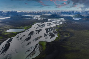 Karanlık volkanik toprak, yeşil yosun, karlı dağlar ve renkli gökyüzünün altında küçük bir göl ile İzlanda 'da örülmüş bir nehir sisteminin havadan görünüşü..