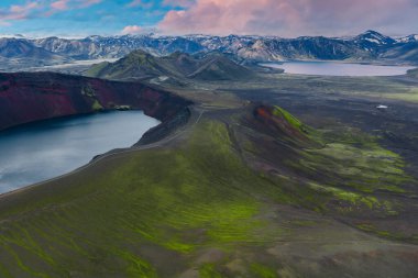 Yosun kaplı tepelerin havadan görünüşü, göllü kırmızı volkanik krater, uzak göl, karlı dağlar, ve İzlanda 'da pastel gökyüzü..
