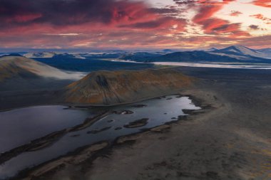 İzlanda 'da volkanik bir kraterin havadan görünüşü. Karanlık arazi, yansıtıcı göller ve parlak günbatımı gökyüzü altında karla kaplı dağlar..