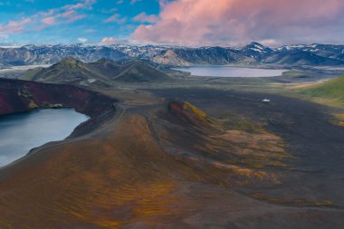 Gökkuşağı renkli tepeler, kraterler, iki göl, engebeli arazi ve renkli gökyüzü altında karla kaplı dağlarla İzlanda 'nın volkanik manzarası..
