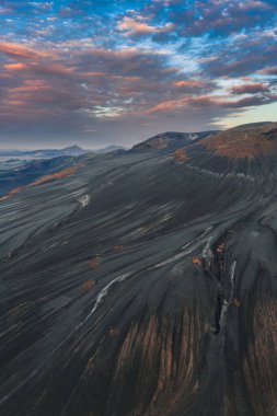 İzlanda 'nın volkanik arazisinin dramatik hava manzarası kül kaplı yamaçlar, kızılımsı kahverengi kayalar ve parlak günbatımı gökyüzünün altındaki uzak dağlar..