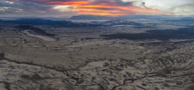 İzlanda 'nın lav sahalarının geniş hava manzarası, kıvrımlı dereler, uzak dağlar ve canlı turuncu ve pembe günbatımı gökyüzünün altındaki buzullar..
