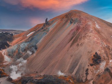 İzlanda 'nın Landmannalaugar bölgesinde, güneş doğarken veya batarken pembe ve turuncu bir gökyüzüne karşı uzanan, kar yamaçları ve buhar delikleriyle dolu renkli yamaçlar..