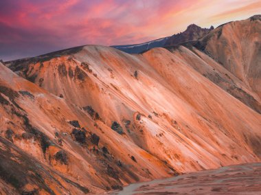 Landmannalaugar, İzlanda 'da pembe ve mor gökyüzü ve volkanik kaya parçalarıyla dramatik bir günbatımı altında çok renkli rhyolite dağları.