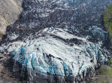 İzlanda 'da beyaz ve mavi buz çizgileri, koyu volkanik kül, dik kayalık uçurumlar ve dramatik bir kontrastlık yaratan yeşil bitki örtüsü olan bir buzul..