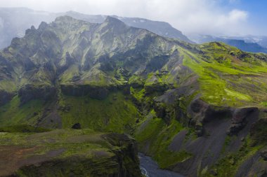 İzlanda 'da yemyeşil bir kanyon yosun kaplı uçurumlar, dolambaçlı bir nehir ve bulutlarla kısmen gizlenmiş sisli dağ zirveleri..