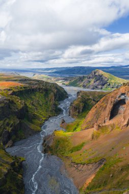 İzlanda 'daki Mulagljufur Kanyonu' nun havadan görünüşü, kıvrımlı bir nehir, yeşil bitki örtüsü olan sarp kayalıklar ve bulutlu bir gökyüzünün altındaki uzak dağlar..