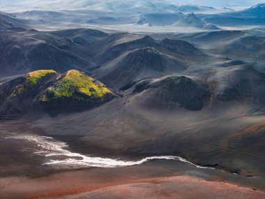 Kraterlerin, tepelerde yeşil yosunların ve ön planda dolambaçlı beyaz bir nehrin bulunduğu İzlanda 'nın karanlık volkanik arazisinin dramatik hava manzarası..