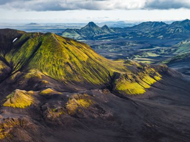 İzlanda 'da karanlık volkanik arazilerle çevrili yeşil bir yosun bulutlu bir gökyüzünün altında tepe, tepe ve vadilerle çevrili..