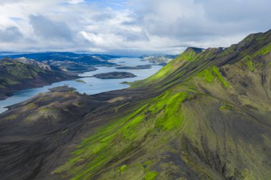 Yeşil yosun manzarası İzlanda 'da koyu volkanik arazi ve tepeleri kaplıyordu. Uzun göller ve sarp dağ sırtları parçalı bulutlu bir gökyüzünün altında..