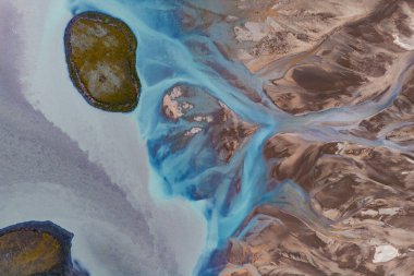 İzlanda 'da parlak mavi sularla örülmüş bir buzul nehrinin hava görüntüsü, engebeli kahverengi arazi, ve odak noktası olarak iki yosun kaplı ada..