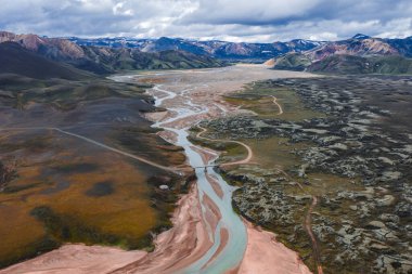 Renkli rhyolite dağları, yosunlu bitki örtüsü ve İzlanda 'nın Landmannalaugar bölgesindeki volkanik kayalar arasında kıvrılan örülmüş bir nehrin havadan görünüşü..