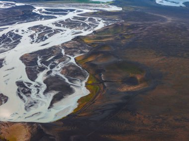 Örgülü nehir kanalları İzlanda 'daki karanlık volkanik arazide akar. Küçük kraterler ve yeşil bitki örtüsü dramatik manzaraya doku ekler..