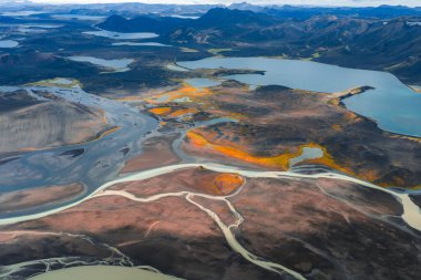 İzlanda 'da göller ve engebeli dağlarla çevrili turuncu ve sarı renkli volkanik arazide akan örülmüş nehirlerin hava görüntüsü..