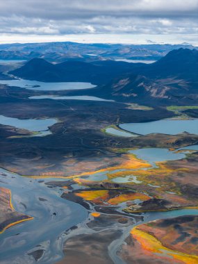 Sarmal nehirlerin hava manzarası, sarı ve yeşil renkli canlı yosunlar, dağınık göller, volkanik tepeler ve İzlanda 'da bulutlu bir gökyüzünün altındaki uzak dağlar..