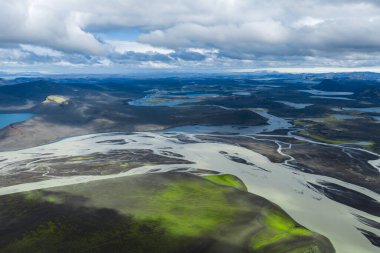 Yeşil yosun kaplı tepeler, uzak göller, kraterler ve bulutlu bir gökyüzünün altındaki dağlar ile örülmüş nehirlerin hava perspektifi..