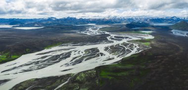 İzlanda 'da örülmüş nehir sisteminin hava manzarası volkanik arazi, yeşil yosun, karlı dağlar ve bulutlu gökyüzünün altındaki uzak göller ile çevrili..