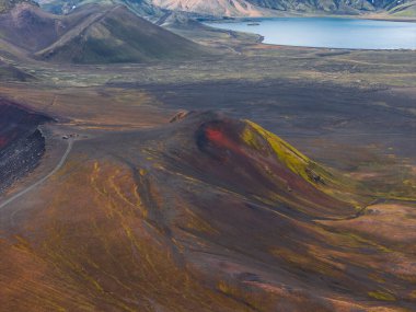 Yeşil yosunlu, kızıl kahverengi bir volkanik kraterin havadan görünüşü, çorak ovalarla çevrili ve engebeli tepelerle çevrili sakin mavi bir göl..