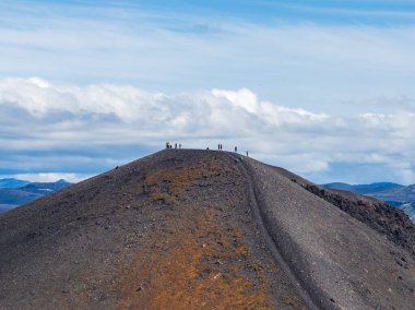 İzlanda 'da, dağcıların zirvede olduğu çorak bir volkanik tepe, karanlık volkanik toprak, turuncu kahverengi alanlar, dar bir patika ve uzak sıradağlar..