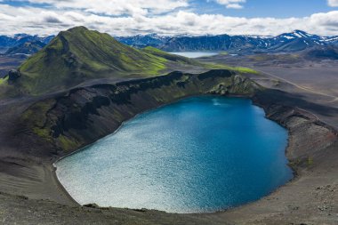 Karanlık arazi, yeşil yosun, dik bir dağ, karla kaplı zirveler ve uzak buzullarla çevrili derin mavi sularla çevrili bir volkanik krater gölü..