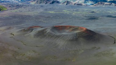 İzlanda 'da volkanik bir krater, koyu toprak, yeşil yosun, engebeli tepeler, uzak dağlar ve buzul izleri ile çevrili kırmızımsı bir çember..