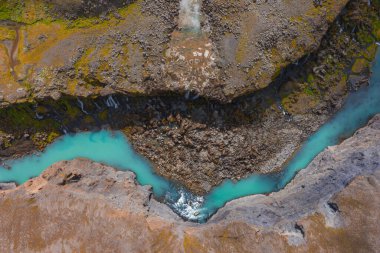 Turkuaz nehri İzlanda 'da engebeli bir kanyon boyunca esiyor, kanyon duvarlarında yosun yamaları ve erozyon desenleri olan kayalık arazilerle çevrili..