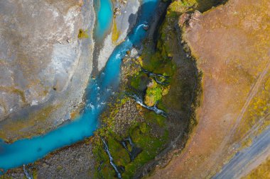Turkuaz nehir, İzlanda 'da yosun kaplı kayalar ve toprak arazide esiyor. Küçük şelaleler nehre dökülür ve dinamik bir hareket yaratır..