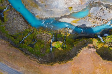 Turkuaz nehri Sigoldugljufur kanyonu yakınlarındaki engebeli İzlanda arazisinde esiyor, yosun kaplı arazi ve çağlayan şelalelerle çevrili..