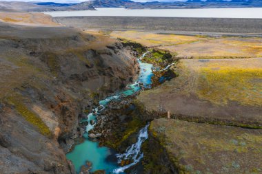 İzlanda 'daki Sigoldugljufur Kanyonu' nda bir turkuaz nehri esiyor, yosun kaplı uçurumlar, küçük bir şelale, uzak bir göl ve görülebilir dağlar var..
