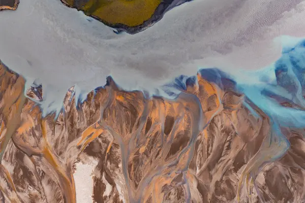 İzlanda 'da örülmüş bir nehir sisteminin hava görüntüsü, turuncu, kahverengi ve mavi renkte, manzaranın üstünde yeşil bitki örtüsü var..