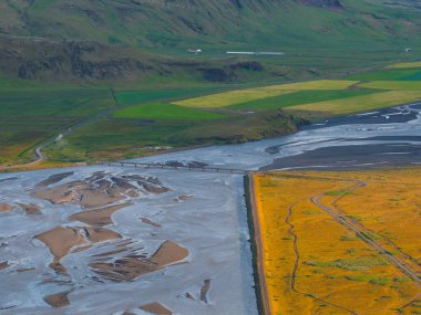 Güneş batarken İzlanda 'da ipeksi kanallar, bir köprü, sarı tarlalar, yeşil tarım arazileri ve engebeli tepeler ile örülmüş nehir sisteminin havadan görüntüsü..