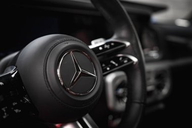 Üç köşeli yıldız logosunun, dikişli siyah derinin ve krom aksanlı kontrollerin bulunduğu Mercedes Benz direksiyonun yakın görüntüsü.