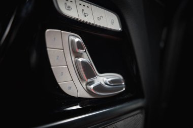 Karanlık lüks bir arabanın içinde, bellek ve ısıtma düğmeleri ile metal koltuk ayarlama kontrolleri, parlak tasarım ve kaliteli işçilik sergiliyor..