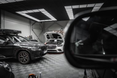 Çatısı olan siyah bir BMW X4 ve kaputu açık beyaz bir Mercedes G sınıfı kareli zemini olan temiz, düzenli bir araba tamirhanesinde..