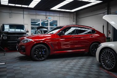 Kırmızı BMW X4, siyah Range Rover Discovery ve Mercedes G Sınıfı modern araba tamirhanesi. Damalı zemin, parlak ışıklandırma ve açık araç kaputları..