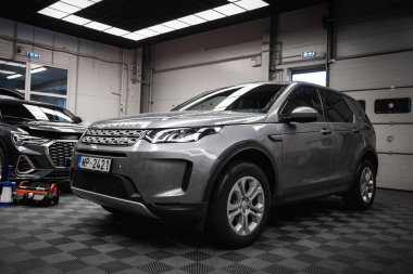 Plakası MP 2421 olan gümüş renkli bir Range Rover Discovery iyi aydınlatılmış bir garaja park edilmiş. Siyah bir BMW X4 ve detay ekipmanları kısmen görülebilir.