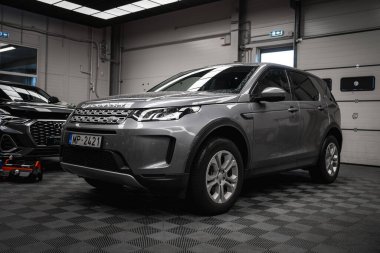 Modern bir garajda park etmiş 2421 plakalı gümüş renkli bir Range Rover Discovery. Yakınlarda siyah ve kırmızı bir araç var..
