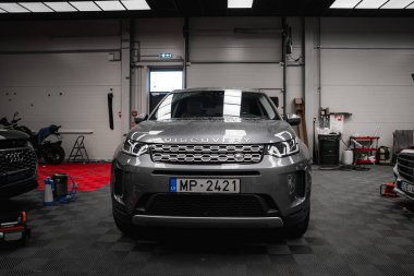 Plakası MP 2421 olan gümüş bir Range Rover Discovery. Arka planda damalı döşeme, aletler ve lüks arabalarla temiz bir garajda sergileniyor..