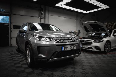 Önünde gümüş rengi Range Rover Discovery olan modern bir garaj ve sağında kaputu açık beyaz bir Mercedes G sınıfı..
