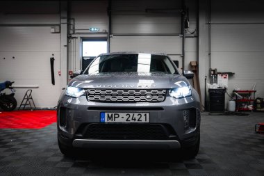 Gümüş Range Rover Discovery siyah ve kırmızı kareli zemini, aletleri, ekipmanları ve kısmen görünür bir motosikleti olan temiz bir garajda park edilmiş..