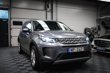 Farları açık gümüş renkli bir Range Rover Discovery ve kaputu açık siyah bir Mercedes G sınıfı kareli zemini olan iyi aydınlatılmış bir garaj..