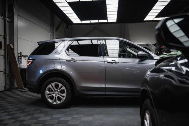 Gümüş rengi bir Range Rover Discovery sanayi tasarımı, aletleri ve siyah bir BMW 'nin parçası ile iyi aydınlatılmış bir garajda kareli bir zemine park edilmiştir..