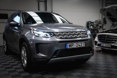 Gümüş Range Rover Discovery, görünür su damlacıkları ve aydınlatmalı farlar Letonya 'nın bir garajına park edilmiş siyah bir Mercedes G sınıfı denetim altında..