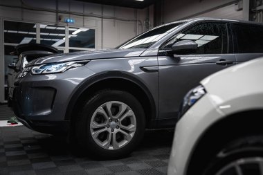 Kiremitli döşemeleri, cam kapıları ve endüstriyel tasarımı olan iyi aydınlatılmış bir garajda park edilmiş gri bir Range Rover Discovery. Beyaz lüks bir araba kısmen görülebilir..