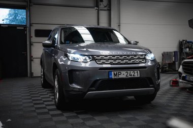 Farları açık gümüş bir Land Rover Discovery, temiz bir garaja park edilmiş döşemeleri döşemeli, parlak ışıklandırmalı ve Letonya 'da görünür atölye araçları.