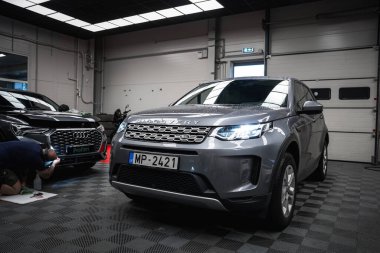 Plakası MP 2421 olan gümüş renkli bir Land Rover Discovery, iyi aydınlatılmış bir garajda. Profilm logosu olan siyah bir Audi sol tarafta kısmen görülebilir..